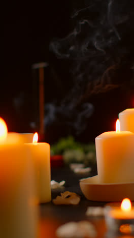 Vertical-Video-Still-Life-Of-Lit-Candles-With-Scattered-Petals-Incense-Stick-Against-Dark-Background-As-Part-Of-Relaxing-Spa-Day-Decor-2